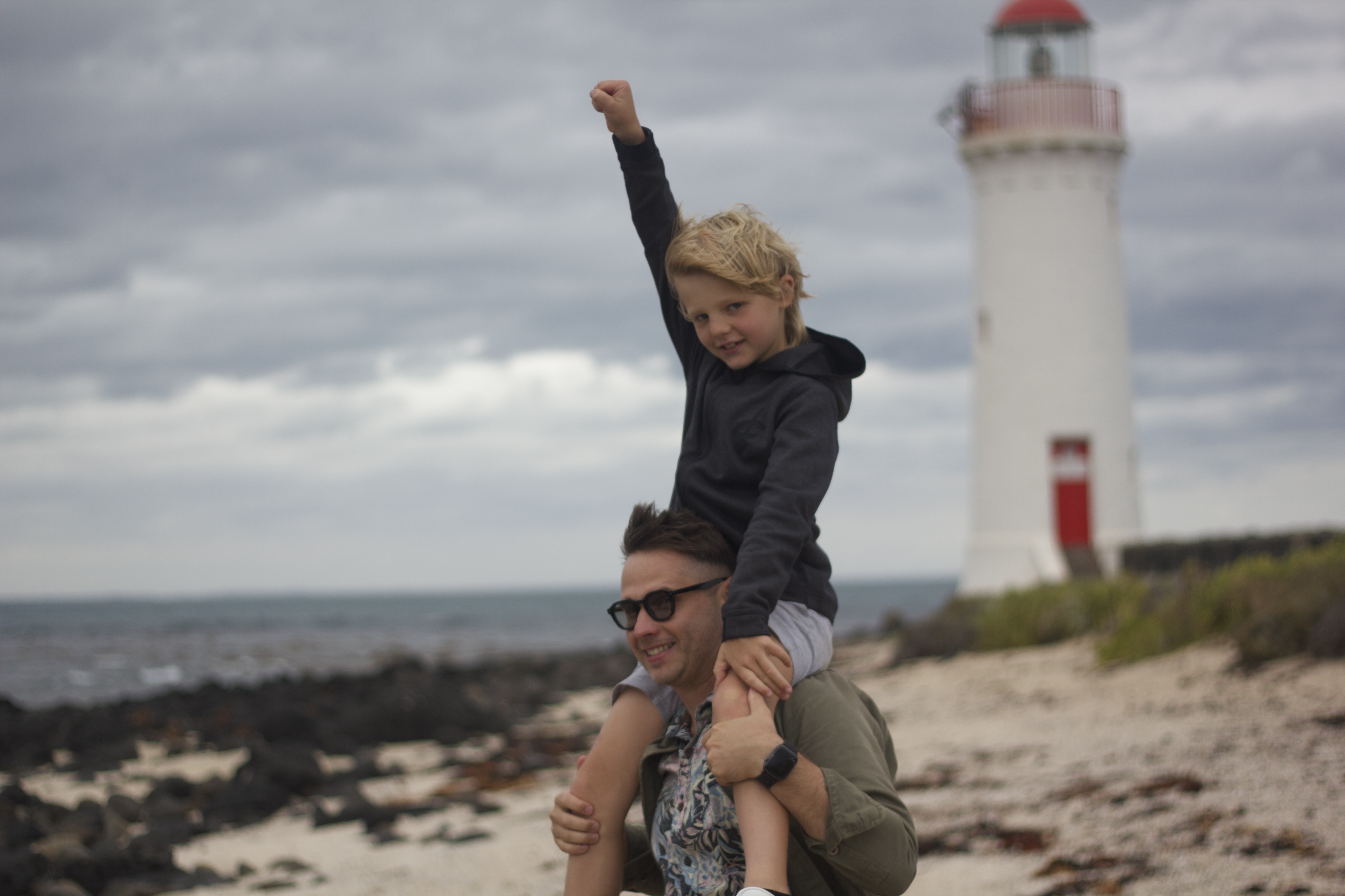 Father carrying son on shoulders at the beach with lighthouse in background